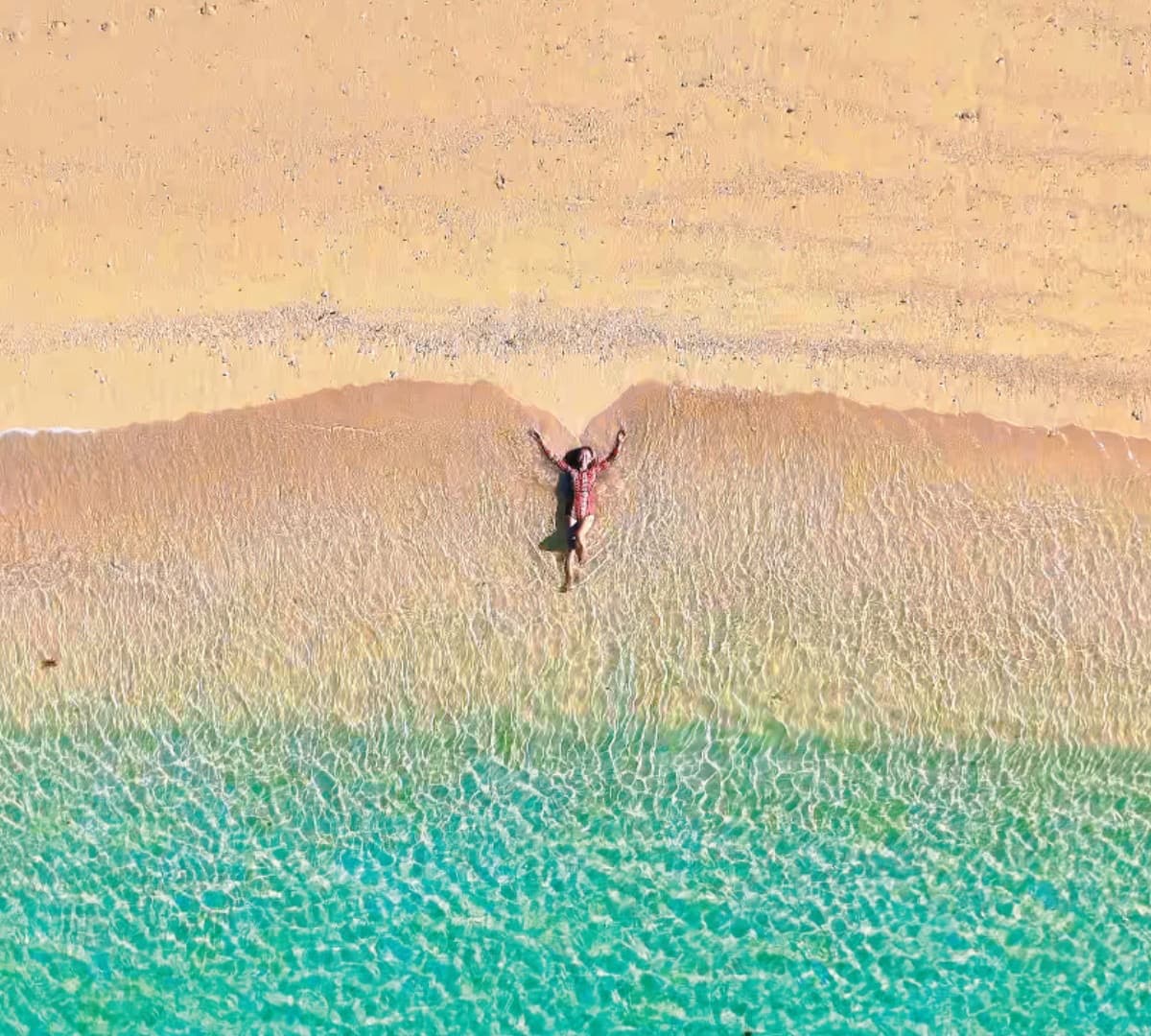 Aerial view of a guest lying in crystal-clear shallows on an empty Okinawa beach