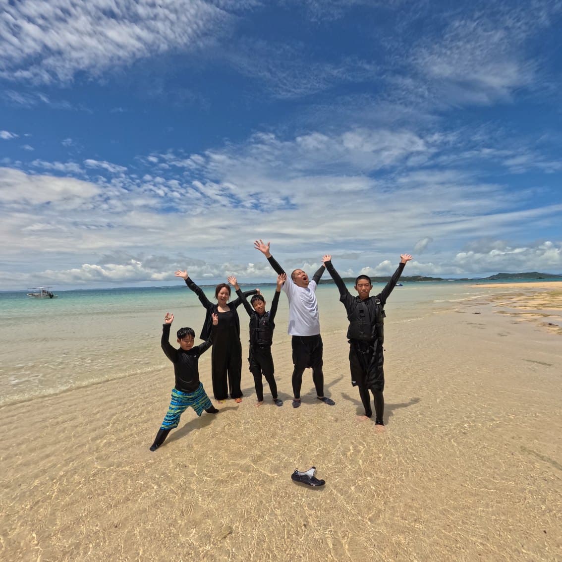 A family on an uninhabited island sandbar, with the private boat behind